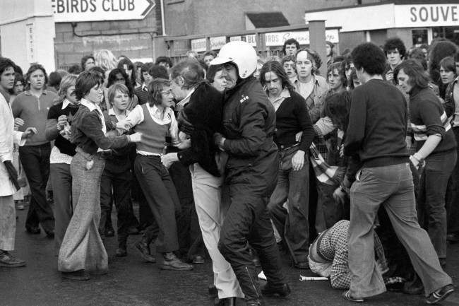 A fan is arrested during scuffles between rival fans, 1970s.