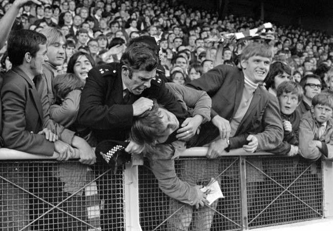 A policeman applies a headlock as he struggles with a youth in the crowd, 1970s.