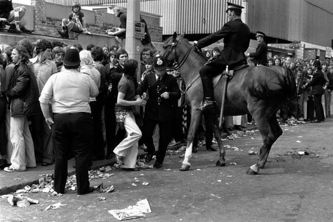 A mounted policeman watches the situation as colleagues deal with crowd trouble, 1970s.