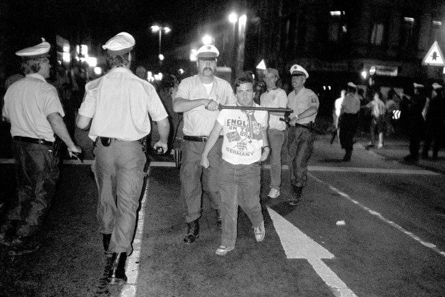 An England fan is led away by a policeman holding a baton to this throat, 1980s.