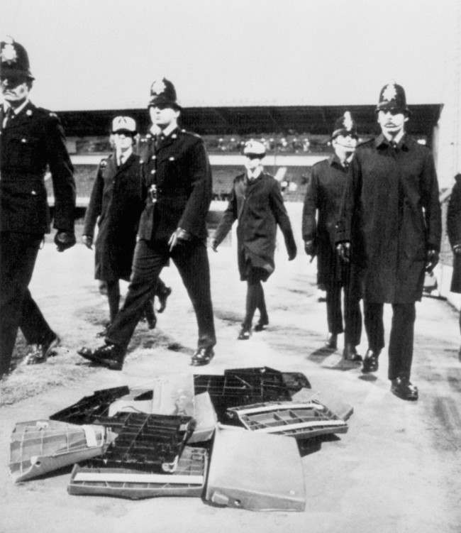 Police officers skirt around a pile of seats thrown from the stands by irate Chelsea fans, 1980s.