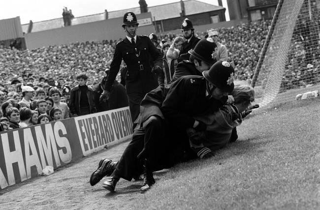 Police wrestle a spectator to the ground, 1980s.