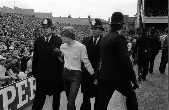 Fans are led away by police after fighting broke out in the crowd, 1980s.