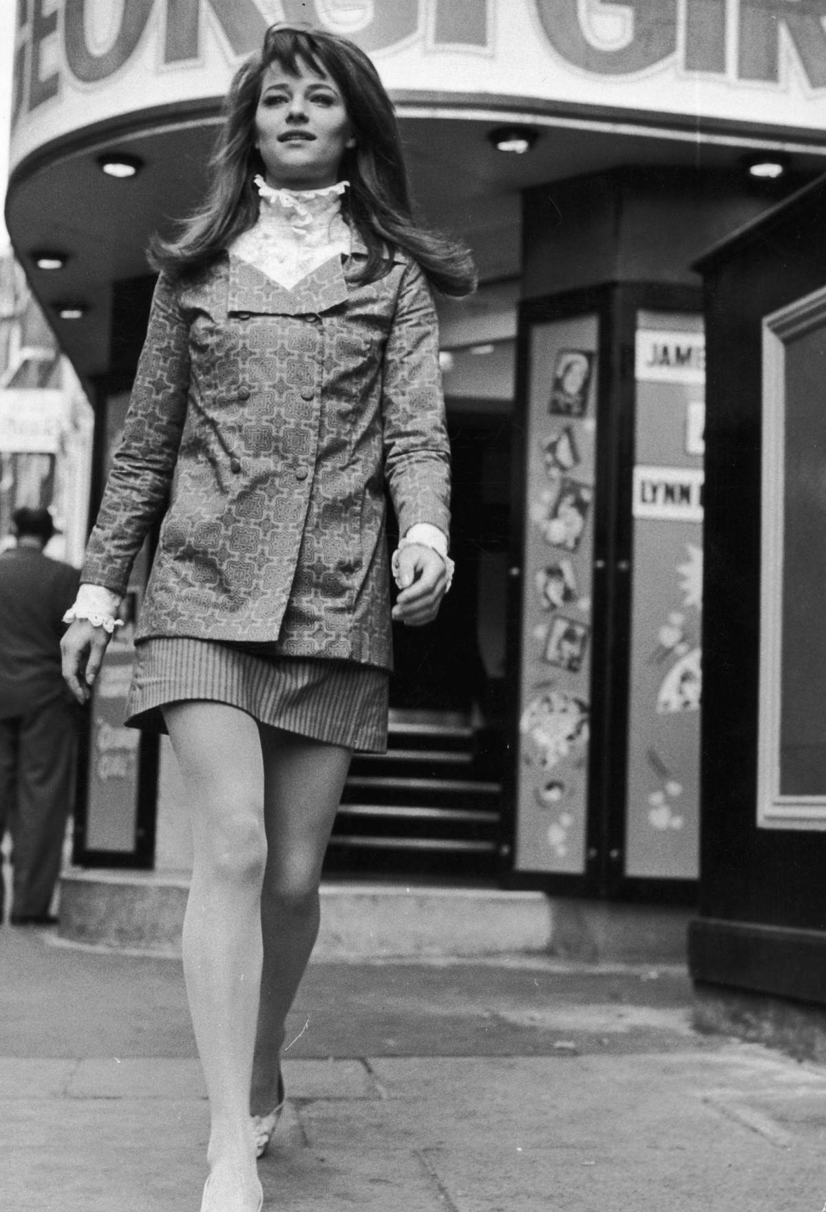 Charlotte Rampling wearing a high-collared Edwardian-style shirt under a double-breasted jacket, and a contrasting striped mini-skirt, 1969