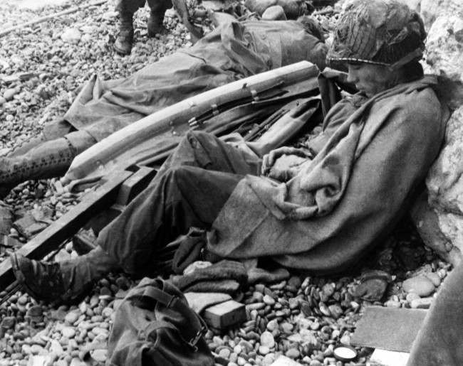 Two American soldiers rest against a chalk cliff on the beach of the Normandy coast of France, 1944.