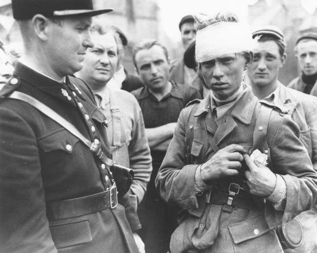 A wounded German soldier who surrendered to the Allied invasion forces, stands surrounded by a crowd of civilians, 1944.