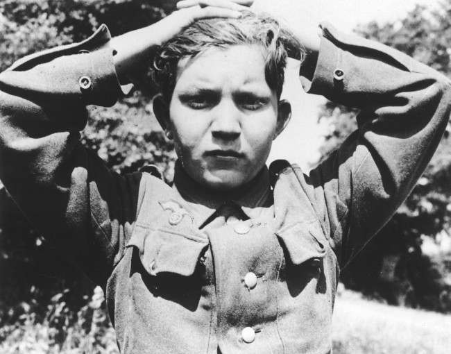 A 16-year old German soldier has his hands clasped over his head as he is taken prisoner, 1944.