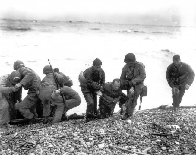 Members of an American landing unit help their exhausted comrades ashore during the Normandy invasion, 1944.