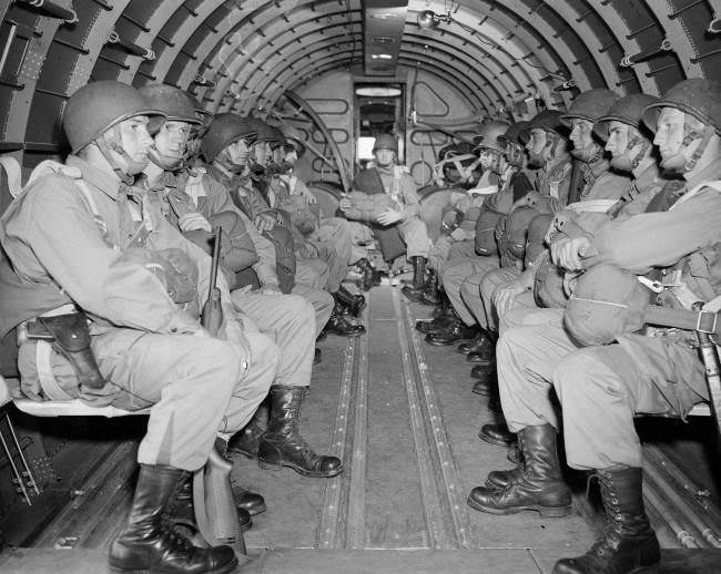 American paratroopers, heavily armed, sit inside a military plane as they soar over the English Channel en route to the Normandy French coast, 1944.