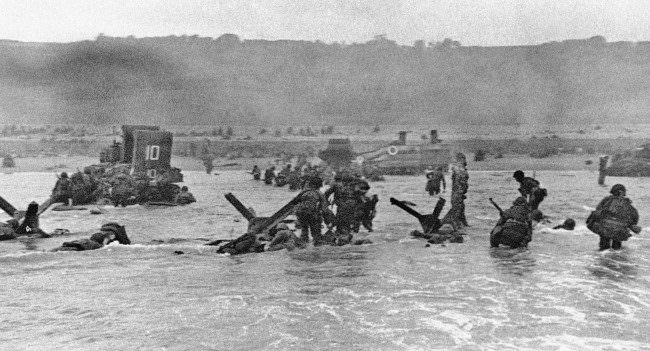 Some of the first assault troops to hit the Normandy, France beachhead take cover behind enemy obstacles to fire on German forces, 1944.