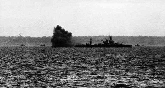 A puff of black smoke blows away from the guns of the USS Arkansas as the might battleship lays down a tremendous barrage, 1944.