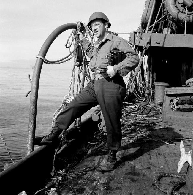 Grant MacDonald, Associated Press war photographer, stands on the deck of a troop transport bound for Kiska. 1943