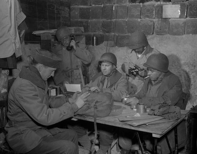 Hal Boyle, Associated Press war correspondent, writes a dispatch on North African fighting. Harrison Roberts, Associated Press photographer, removes film from his camera in an improvised bomb proof field headquarters. 1943