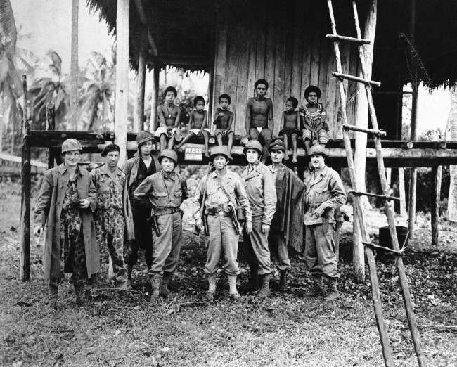 War correspondents covering the allied occupation of Kiriwina Island line up in front of a native hut. 1943