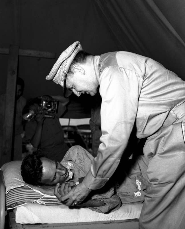 General Douglas MacArthur leans sympathetically over the hospital bed of Vern Haugland, war correspondent of the Associated Press who fought his way out of the New Guinea jungle after being lost for 43 days. General MacArthur awarded Haugland the Silver Star. 1942