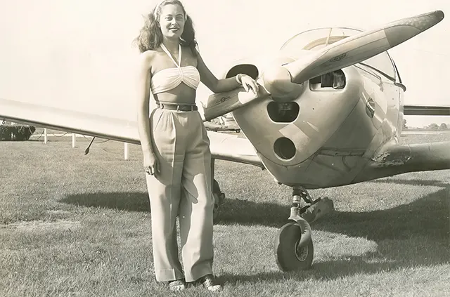 A young woman poses with an airplane, 1940s