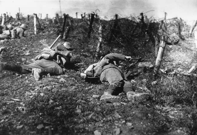 German troops stay close to the ground as one soldier uses pliers to cut barbed-fire fence during World War I.