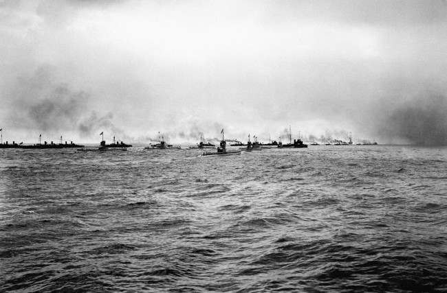 A flotilla of German submarines (U-Boats) and torpedo boats heading out to sea.