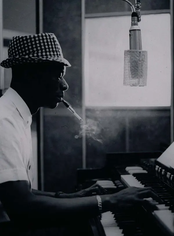 Nat King Cole enjoys a smoke while he plays his tunes on a piano.