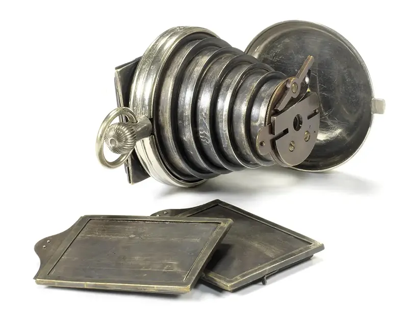 This 1886 device was described as the Improved pattern patent watch camera and is one of the few surviving examples which uses photographic plates, pictured in the foreground, instead of film.