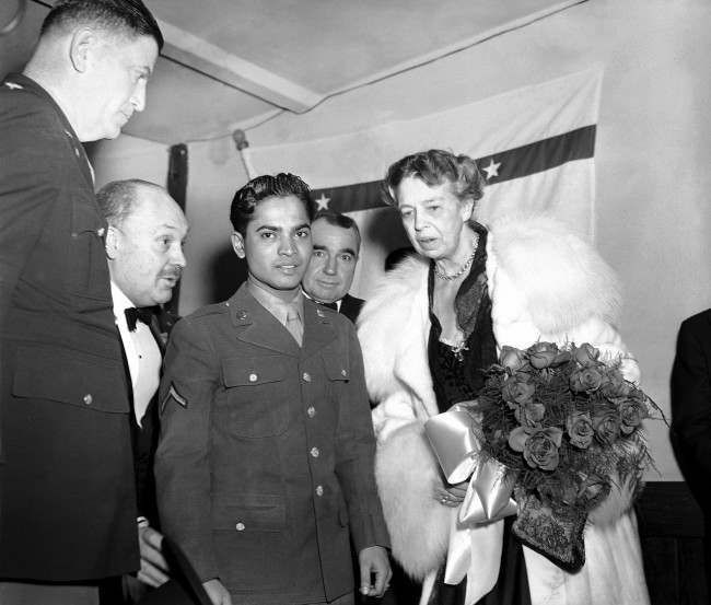 Eleanor Roosevelt holds a bouquet of roses as she stands with Sabu, the ÂElephant BoyÂ of movie fame, and now a soldier attached to Fort Meade, Md., at the president’s birthday ball celebration at a USO post in the YMCS in Washington on Jan. 29, 1944.