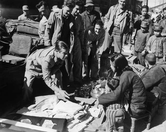 Joe E. Brown, the wide-mouthed movie comedian, drives a bargain with a Chinese street merchant as American soldiers and Chinese youngsters look on, during his tour of China, Jan. 10, 1944.