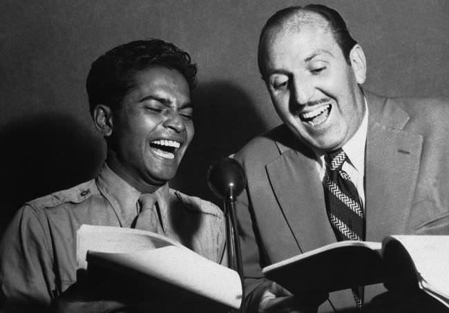 Well known film star, Sabu, Staff Sergeant Sabu Dastagir, now serving as an aerial gunner attached to the 13th U.S. Air Force on active service in the Pacific, gets a laugh from Bob Dyer, radio comedian, as Sabu rehearses for a radio show, while on leave in Sydney, New South Wales on Feb. 27, 1945.