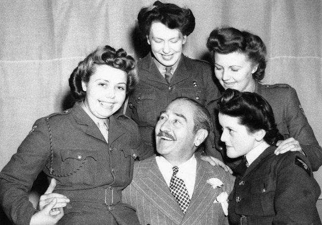 Adolphe Menjou, the famous film star, is seen making friends with three A.T.S. girls and A.W.A.A. girls at his first troop concert in this country June 14, 1943.