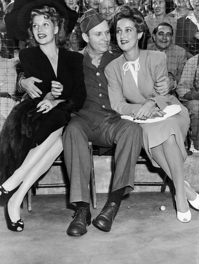 Dressed in the uniform of a technical sergeant of the U.S. Army Air Forces which he joined, Gene Autry, cowboy movie actor, found himself as popular with a pair of glamorous actresses as he is with the kids of the nation when he appeared at a benefit party staged by film actress Marion Davies, Aug. 9, 1942. With him are Rita Hayworth, left, and Dorothy Lamour.