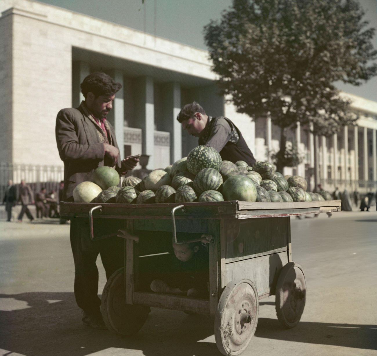 A customer buys a watermelon from a trader at his market stall in front of a bank building in Tehran, the capital of Iran, circa 1960.