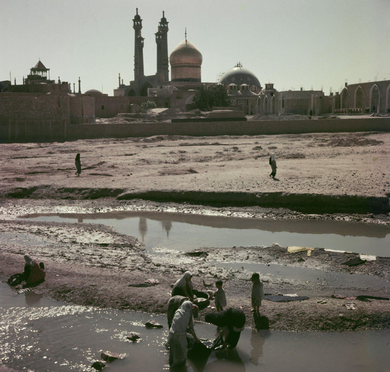 Residents washing clothes in the waters of the Qom River, with the Fatima Masumeh Shrine and Azam Mosque of Qom behind, in the city of Qom, the capital of Qom Province in central Iran, circa 1960.