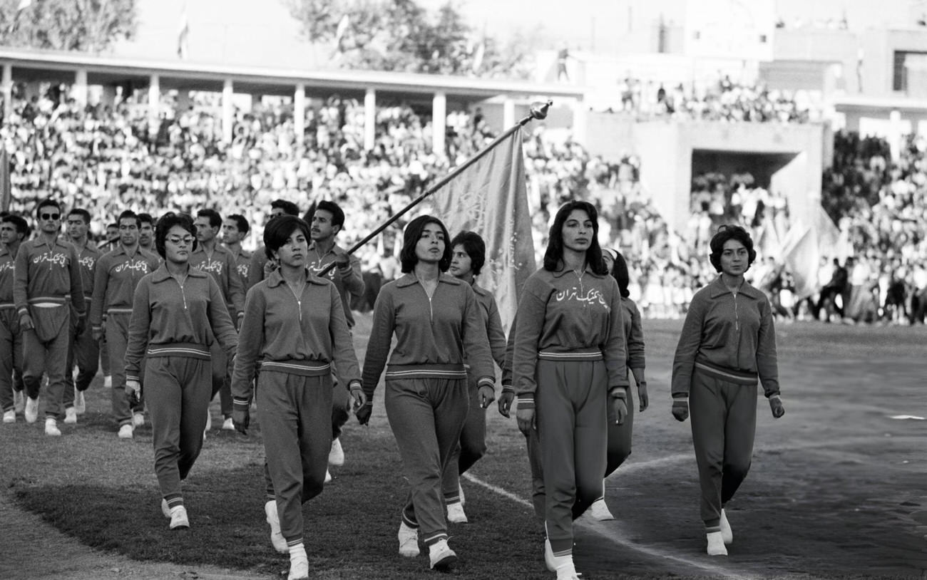 A parade of young people in sports attire hoisting a flag in the stadium for the 42nd birthday of Shah Mohammad Reza Pahlavi, Tehran, 1960.