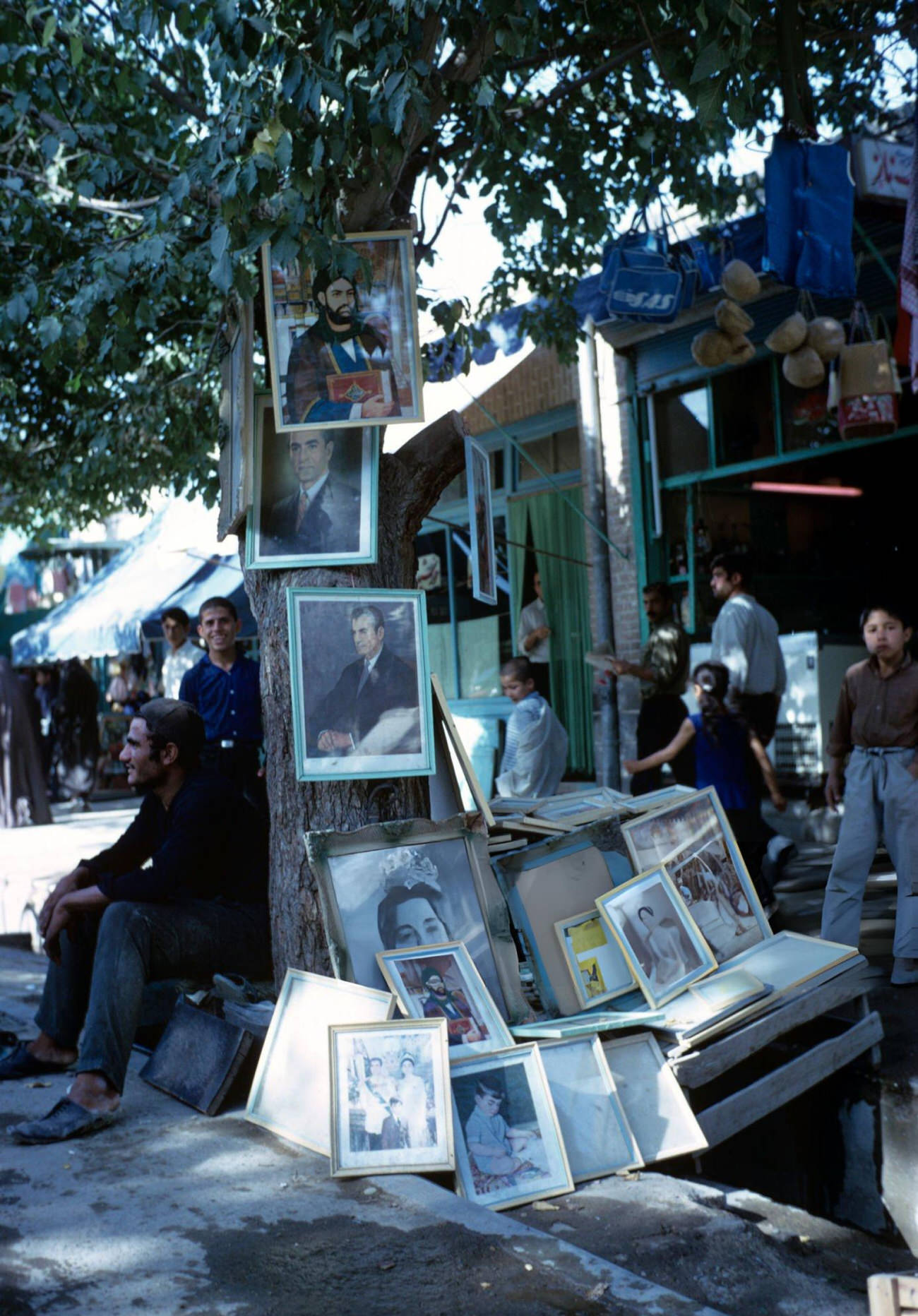 Portraits of the royal family and religious dignitaries hanging on the trunk of a tree in a street in Iran, 1969.