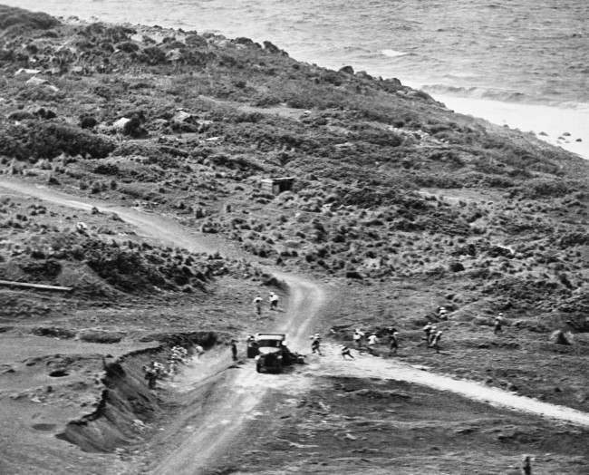 Near a truck on an Iwo Jima road in Japan, Jap soldiers with field packs scatter for cover, as an American plane comes in low to strafe the enemy during pre-invasion softening-up, 1945.