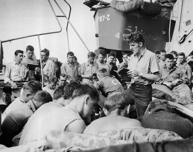 Coast Guardsman Charles R. Roth, leads the singing of hymns on an LST headed for Iwo Jima, the day before the invasion, 1945.