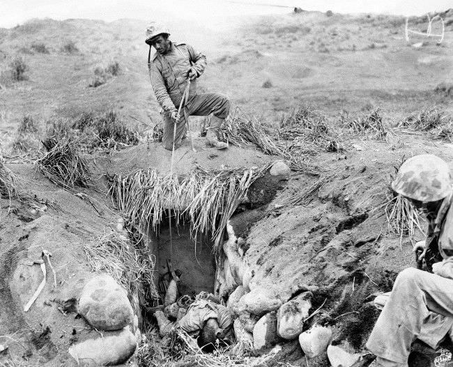 Battle-wise Marines use a sling made of enemy puttees to improvise a sling for the removal of a Japanese soldier’s body from a dugout on Iwo Jima, Japan, 1945.