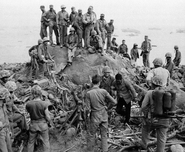 While his buddies stand around to watch, a Third Division Marine brings in a Japanese prisoner, one of the few enemy taken alive during the fighting on Iwo Jima, Japan, 1945.