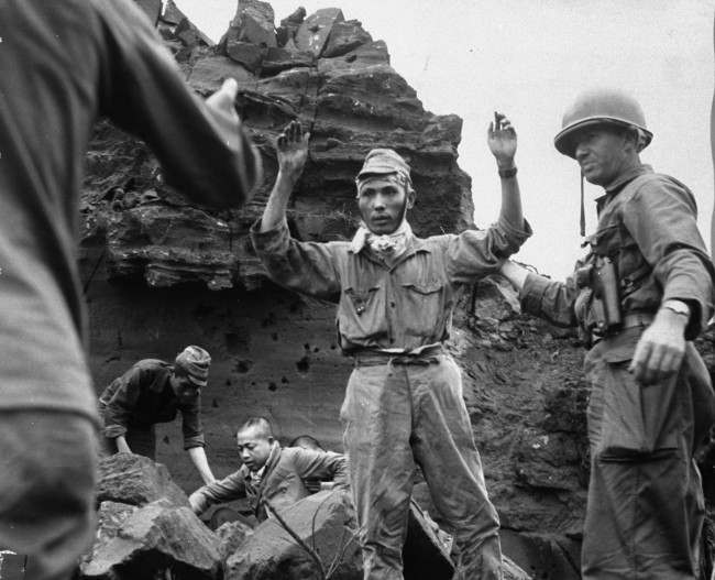 With his hands in the air, the first of 20 Japanese emerges from an Iwo Jima cave, 1945.