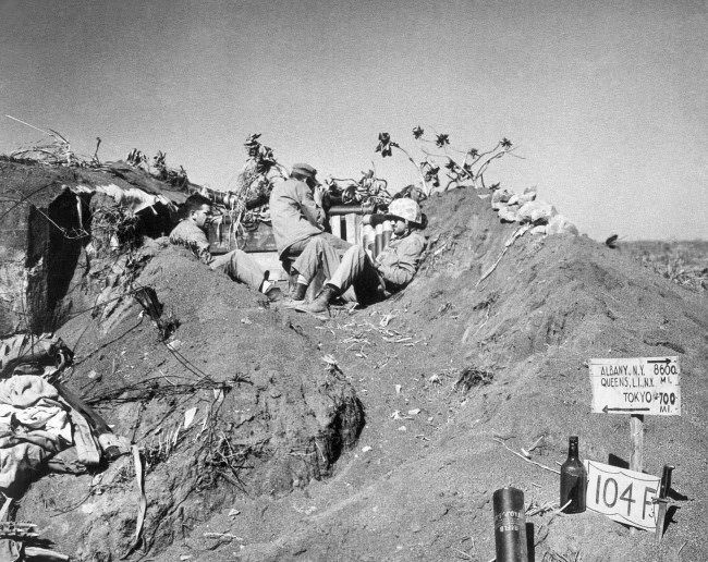 U.S. Marines with a coast guard combat photographer found crouching in a listening post dug in Iwo Jima’s coffee grounds sands, Japan, 1945.