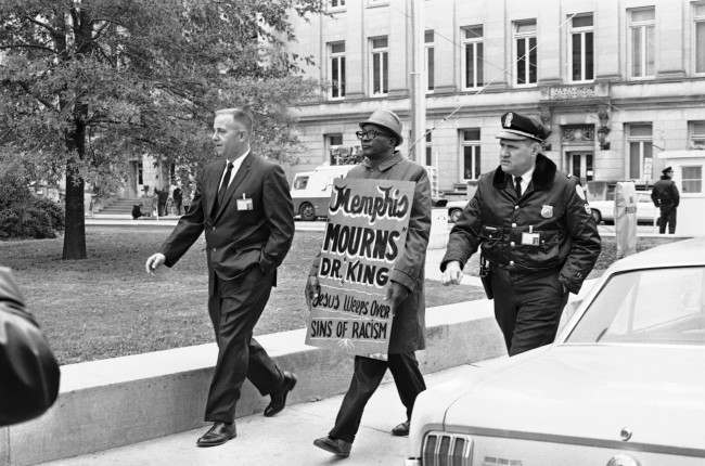 A plainclothes detective and a uniformed Shelby County Deputy sheriff usher away from the Shelby County Jail a picket who attempted to walk the sidewalk around the courthouse in Memphis, Tennessee, 1968.