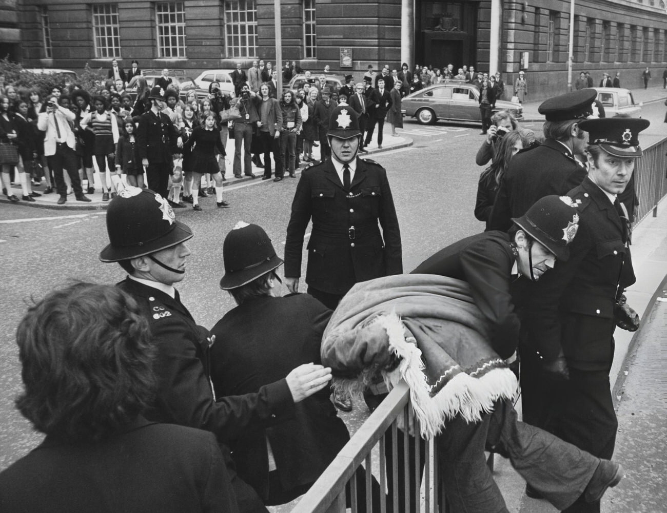 Police officers restrain an Afghan-coated activist during a one-day strike organized by the Schools Action Union protest outside the Greater London Council headquarters at County Hall, 1972.