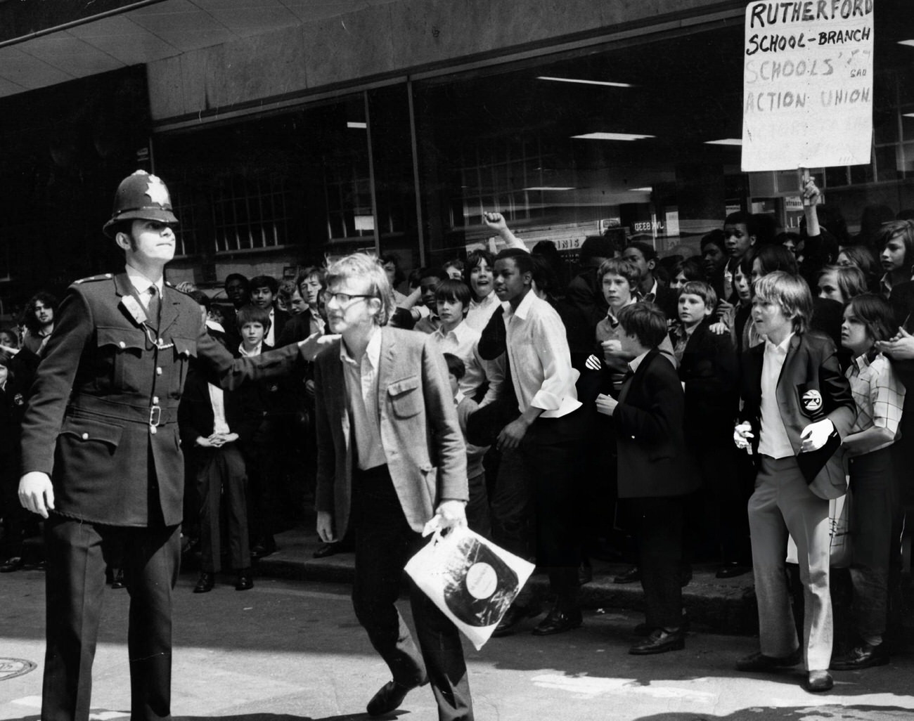 Leader of school strike Steve Finch, aged eighteen, with fellow pupils of Rutherford School, is escorted by a policeman to a meeting in London, 1972.