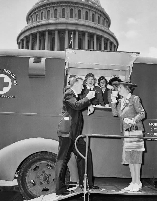 Red Cross workers, demonstrating one of the five mobile canteen units acquired for relief work in the event Washington has an air raid, stop by the Capitol on June 18, 1942, and dish up mugs of coffee for Senator Joseph C. O'Mahoney, left, (D-Wyo.) and Rep. Edith Nourse Rogers, right, (R-Mass.).