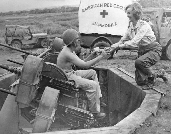 Red Cross worker Roxane Pollack (right), of Philadelphia, Pa., hands coffee and doughnuts to Pfc. Marvin Clover, of Clayton, Ala., as he stands guard at his gun position on the fringe of a Dutch New Guinea air base on Oct. 23, 1944. Mobile canteen of the Red Cross is mode of transportation of the food.