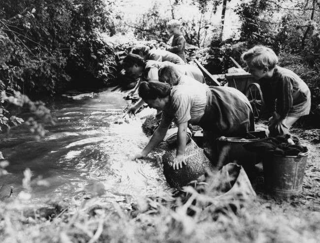 French children watch their mothers wash clothes in a brook in Normandy, 1944, in an area liberated from the Nazis by American Forces.