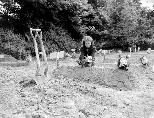 A French girl places flowers over the freshly-dug grave of an American Airborne trooper as a token of appreciation of arrival of Allied liberators on the northern coast of France, 1944.