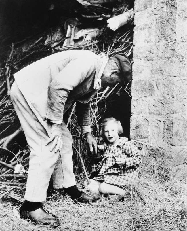 A bright-eyed little French girl is persuaded to leave the spot, behind a pile of branches, where she made her home when the Allies swept into her community in Normandy, 1944.