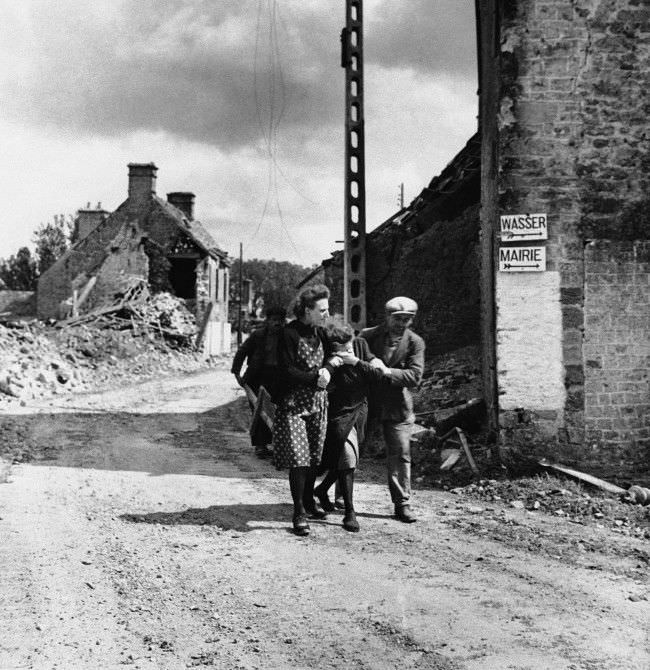 Two friends assist a weeping woman (center) in the Normandy village of Ste. Marcouf, 1944, after her husband was killed when the Germans shelled the place.