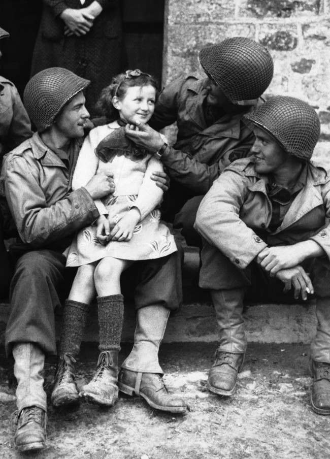 A little French girl finds three admirers from the ranks of American forces who have made a speedy and successful advance through Normandy, France, 1944.