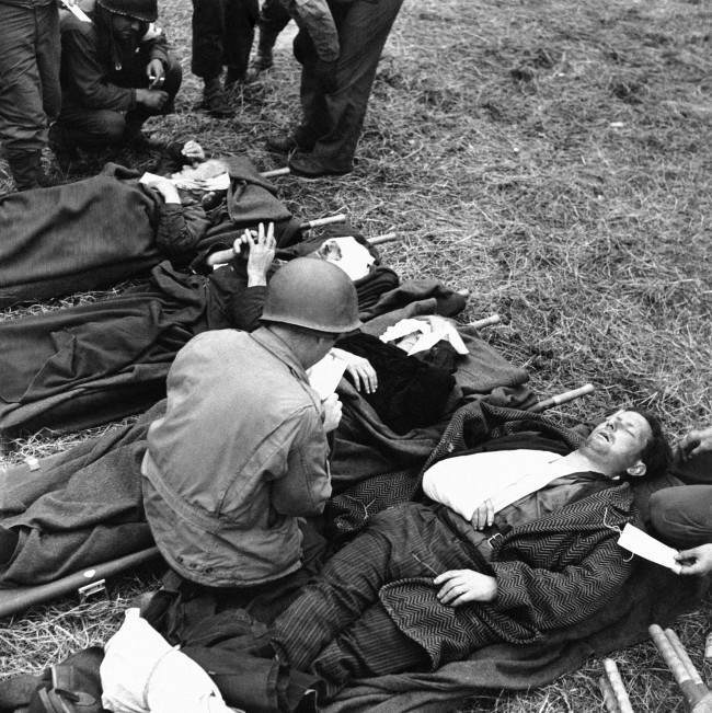 French civilians, wounded during the Normandy battles, 1944, lie on stretchers on the ground behind the lines, where they are treated by U.S. Army medical corpsmen.